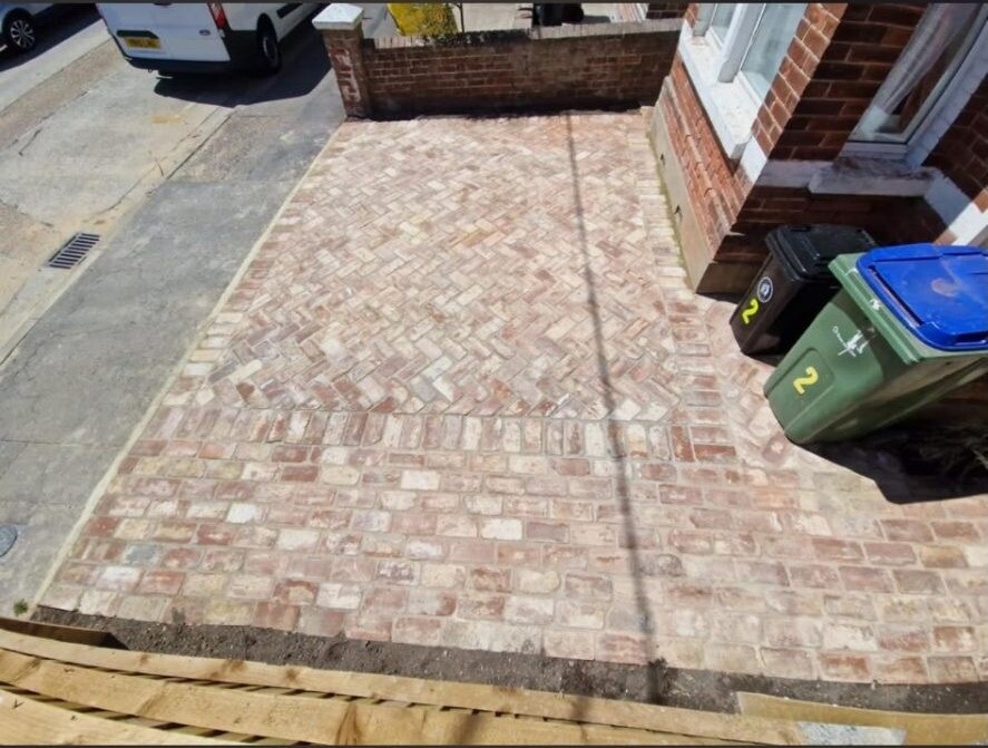 Red clay-brick paving being laid in a herringbone pattern.