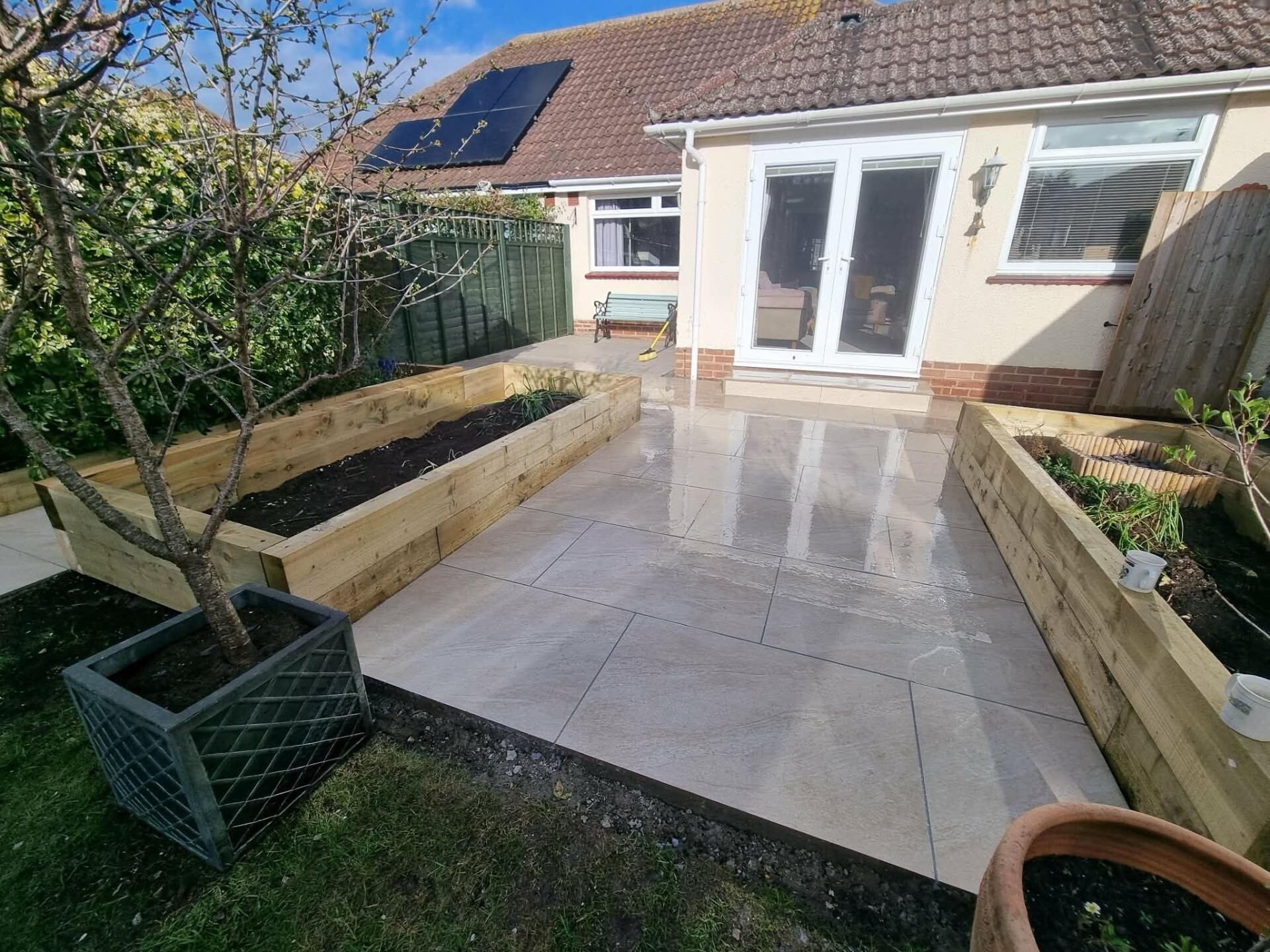 Porcelain patio with timber raised beds at the side of a Sussex property.