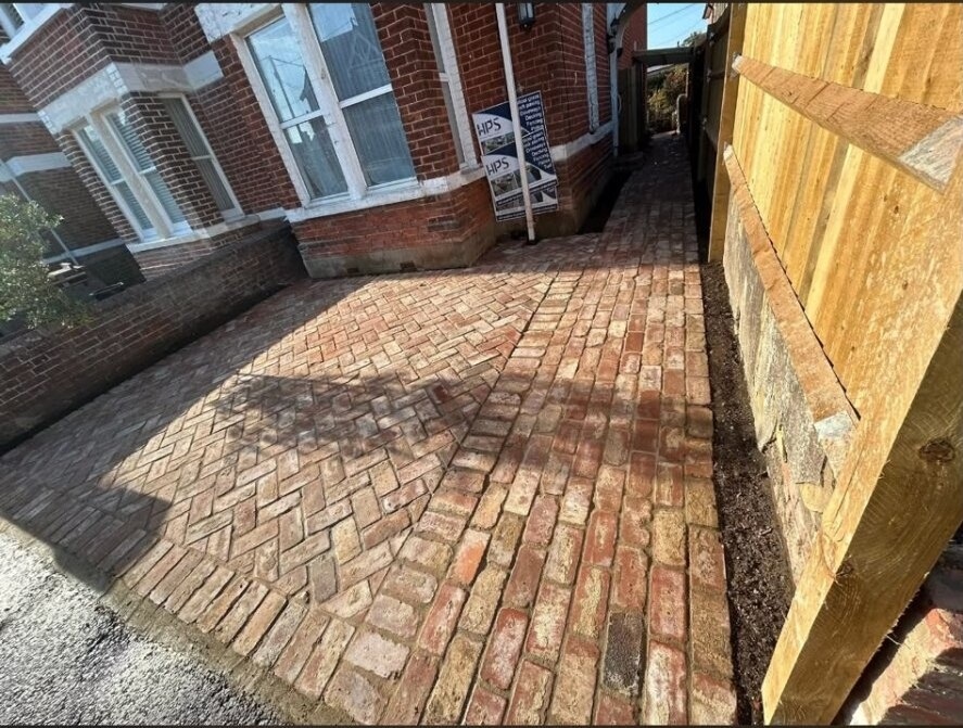 Red clay-brick path bordered by closeboard fencing in a side-return garden.