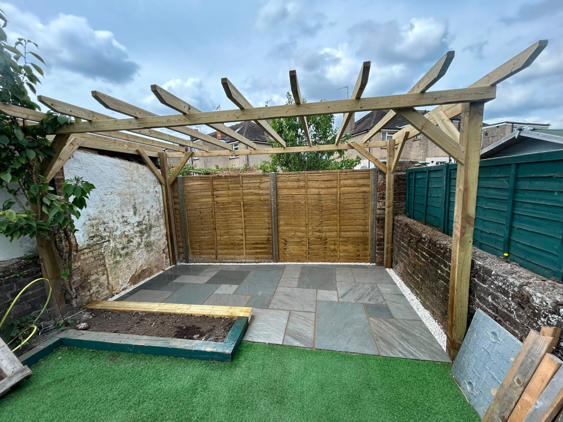 Bespoke timber pergola built over a hand-laid sandstone patio in a West Sussex back garden — installed by Heavens Property Solutions.