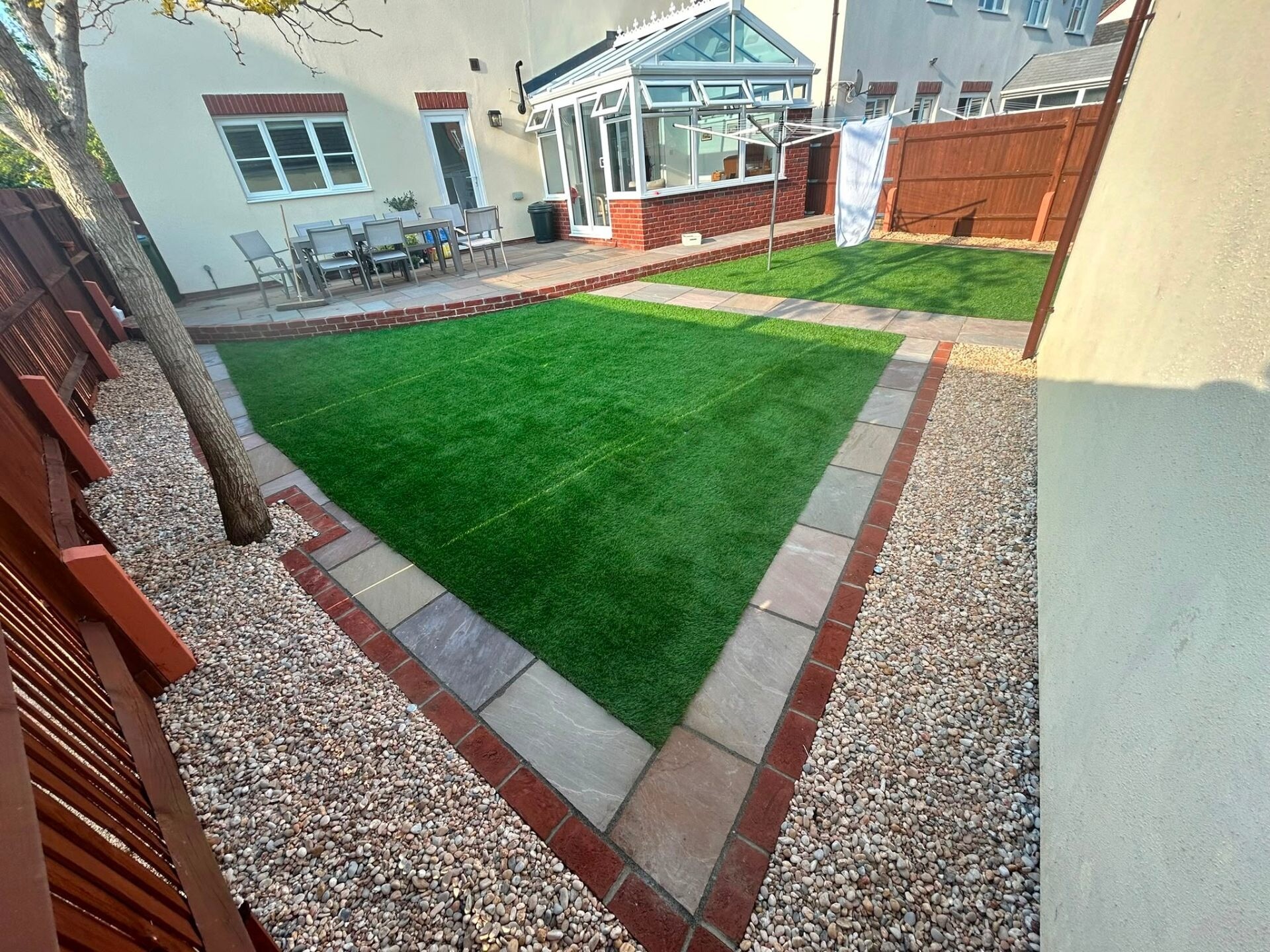 Premium artificial grass lawn framed by a red-brick mowing strip.