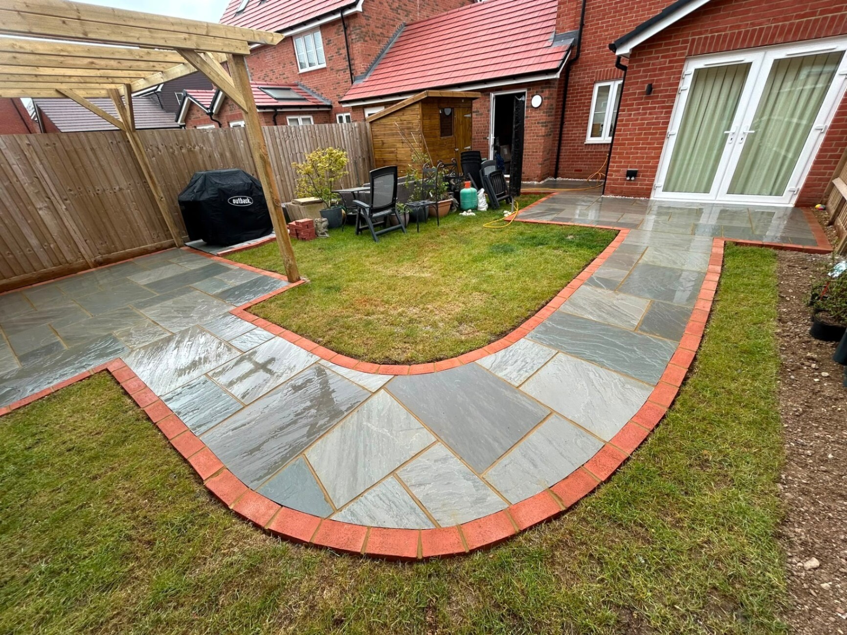 Sandstone patio with red-brick edging curving around a central lawn.